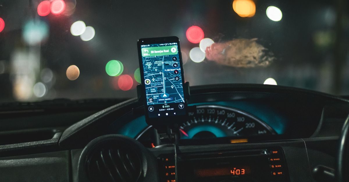 Smartphone fixé sur le tableau de bord d'une voiture affichant un itinéraire GPS de nuit avec des lumières urbaines floues