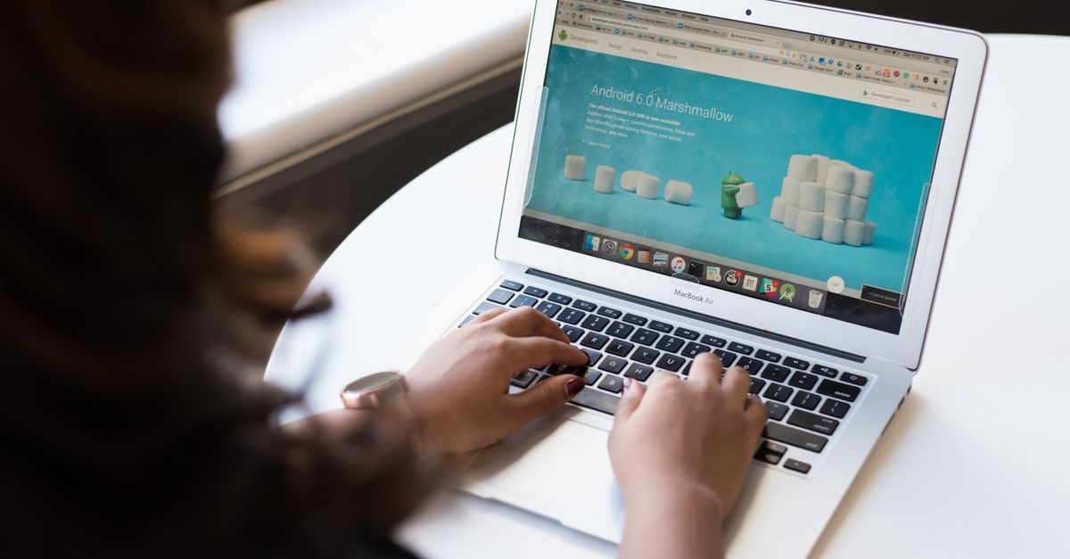 Iemand typt op een laptop met een Android 6.0 Marshmallow-pagina op het scherm aan een witte tafel