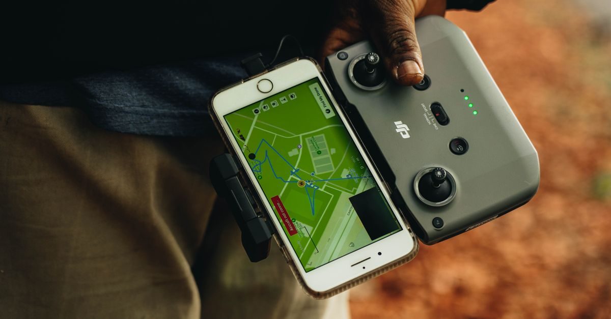 Iemand houdt een drone-afstandsbediening vast met een smartphone waarop een navigatiekaart met een vliegroute zichtbaar is