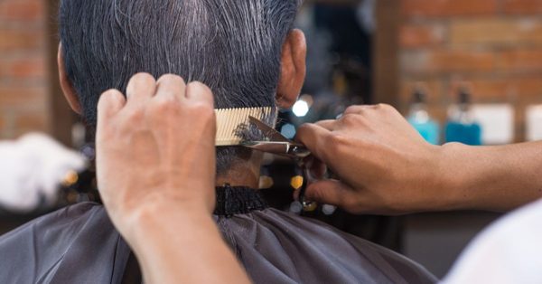 Kapper knipt met schaar en kam het grijze haar van een klant in een kapsalon