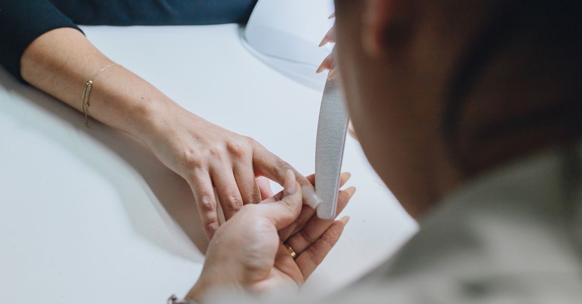 Una manicurista lima las uñas de una clienta sobre una mesa blanca en un entorno profesional y tranquilo