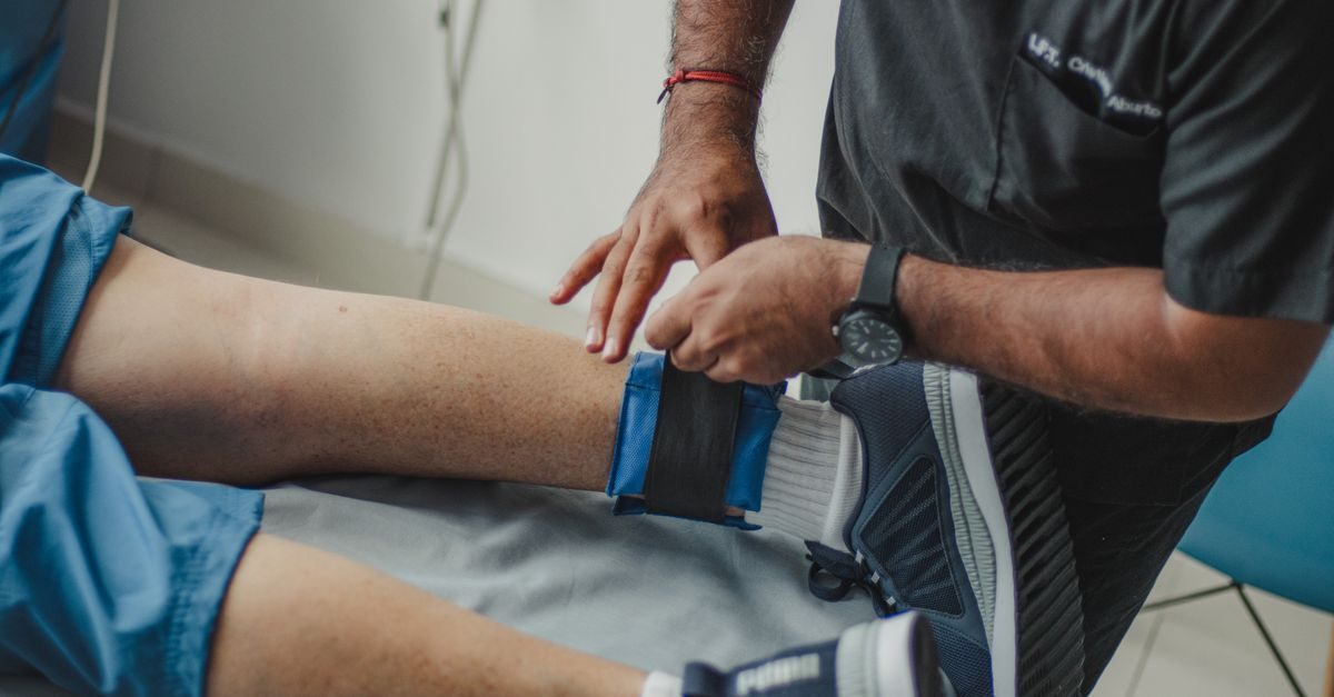 Fisioterapista applica una cavigliera con peso alla gamba di un paziente disteso su un lettino in uno studio medico