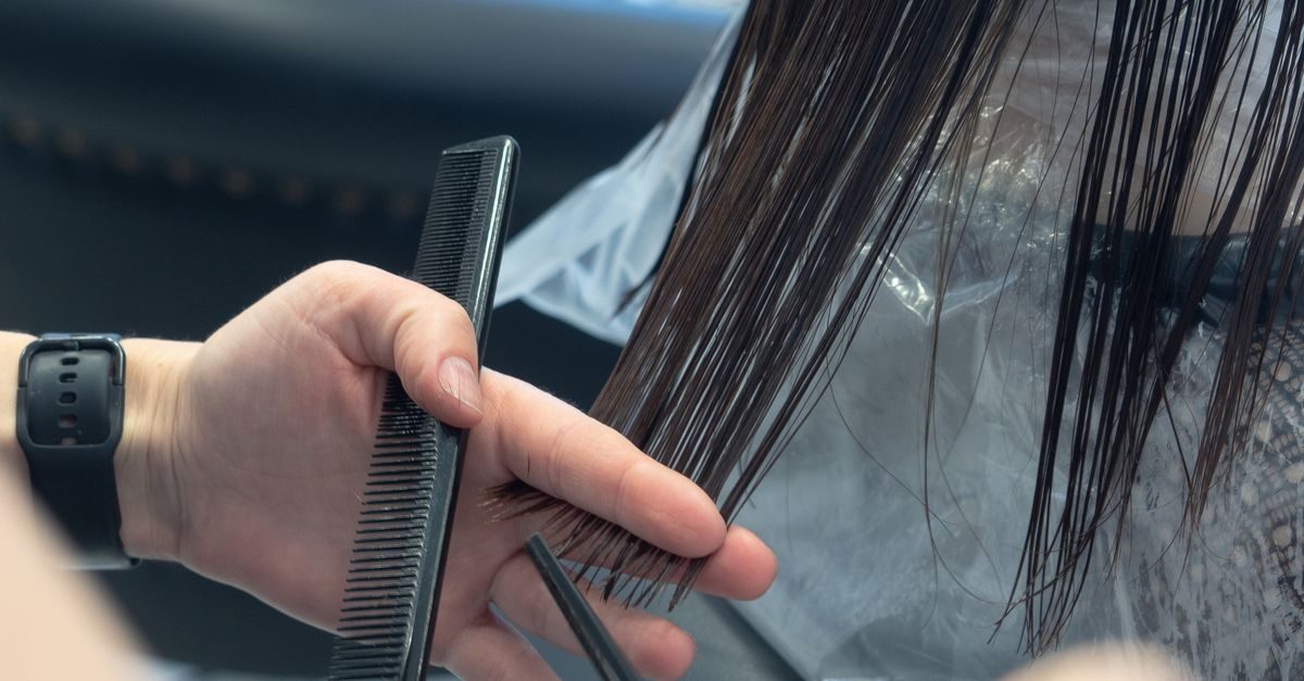 Kapper knipt met een kam en schaar nat donker haar van een klant in een kapsalon