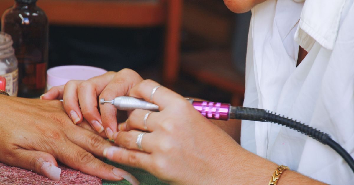Manicurista profesional utiliza un torno eléctrico para limar las uñas de una clienta en un salón de belleza
