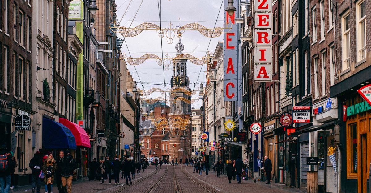 Drukke winkelstraat in Amsterdam met historische toren, verlichte kerstversiering en voorbijgangers op straat