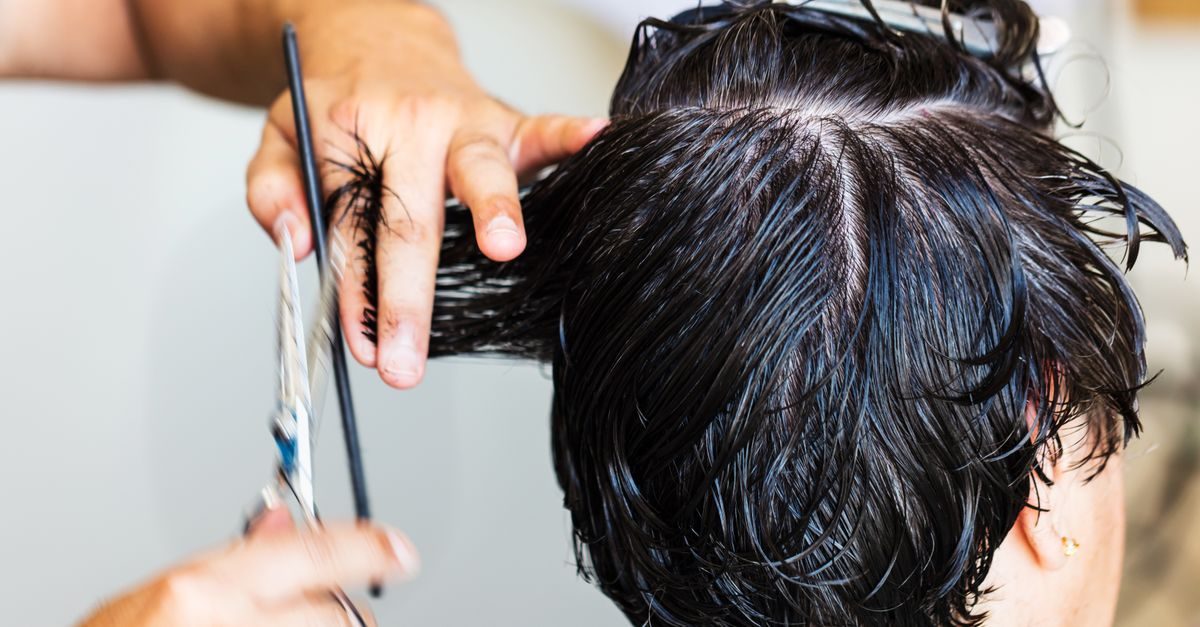 A hairdresser uses scissors and a comb to trim a client's wet, dark hair in a professional salon setting