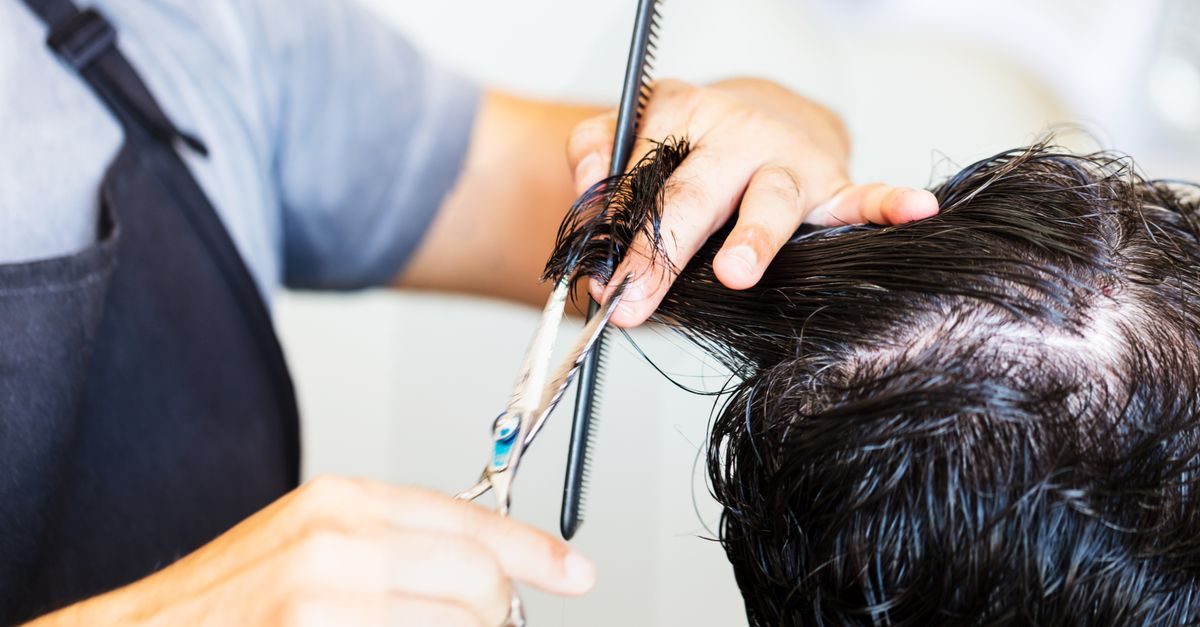 Un parrucchiere taglia i capelli scuri e bagnati di un cliente usando forbici e pettine in un salone professionale
