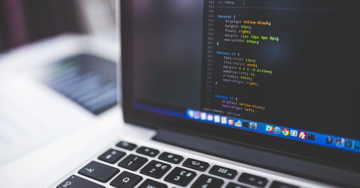 Nahaufnahme eines Laptops mit sichtbarem Programmiercode auf dem dunklen Bildschirm und geöffneter Taskleiste
