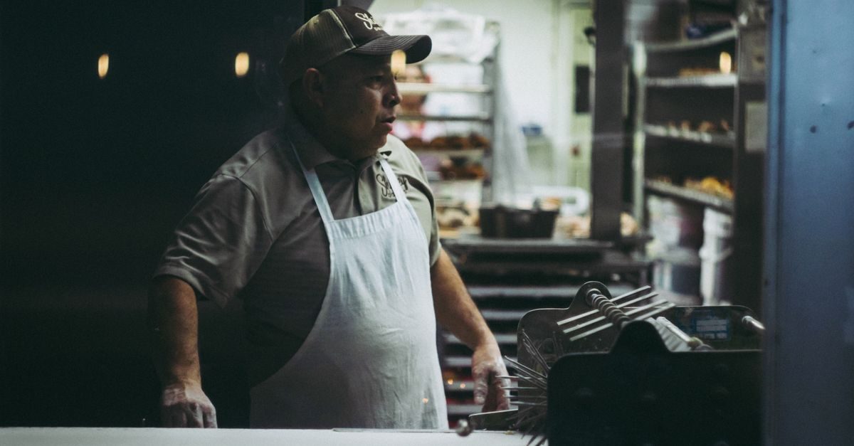 Un boulanger portant une casquette et un tablier blanc travaille dans son atelier sombre et chaleureux
