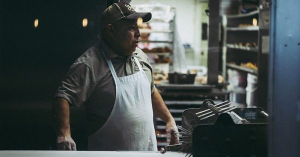 Un boulanger portant une casquette et un tablier blanc travaille dans son atelier sombre et chaleureux