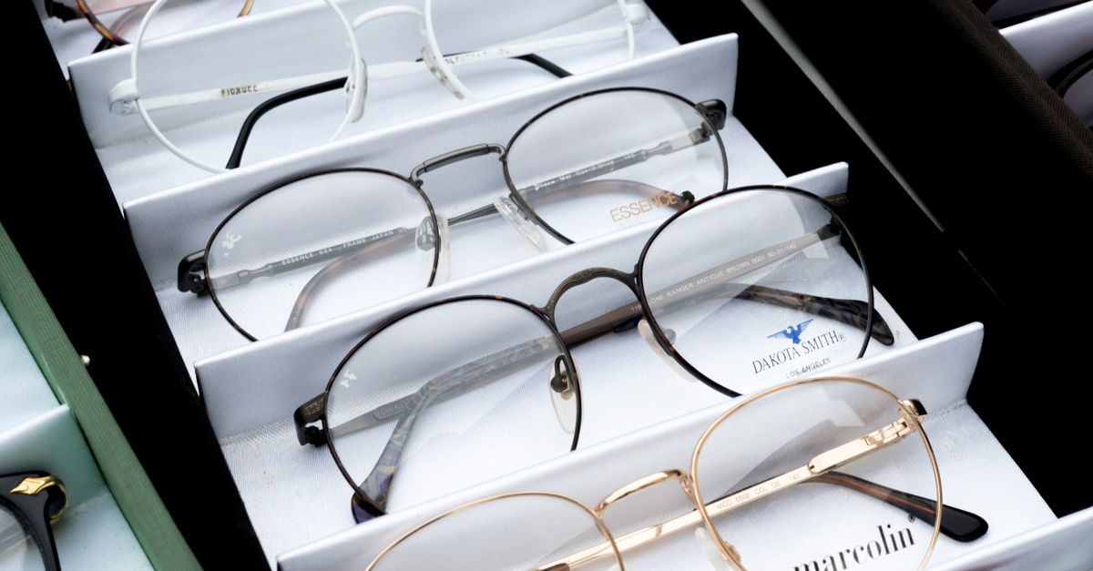 Plusieurs paires de lunettes de vue aux montures variées sont soigneusement alignées dans un présentoir blanc chez un opticien