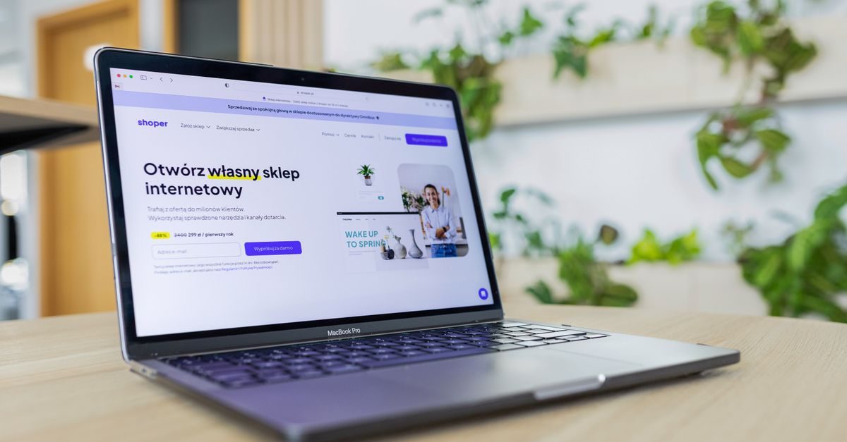 Laptop screen displaying a Polish e-commerce website on a wooden desk with blurred green plants in the background