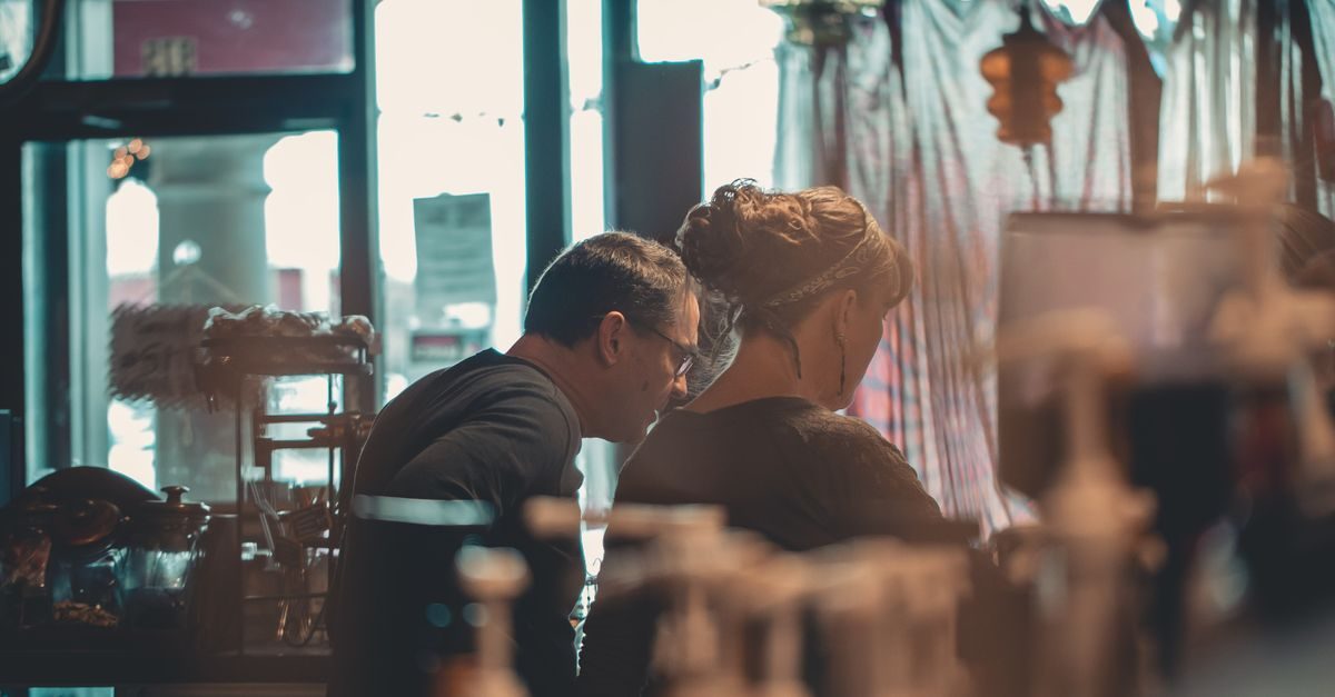 A man and woman sit side-by-side in a softly lit, cozy room, looking down together at a shared screen or document
