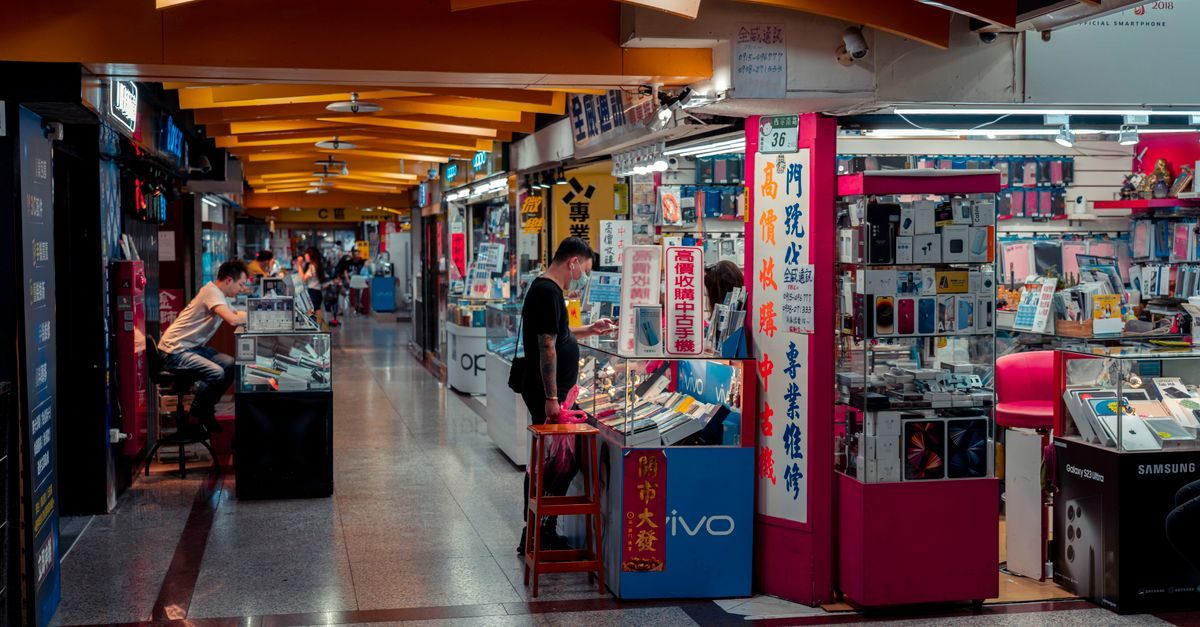 Mensen in een Aziatische winkelpassage met kleine elektronicawinkels en vitrines vol smartphones en accessoires