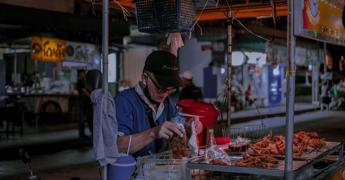 Un vendeur de rue concentré prépare des sachets de nourriture frite sur son stand nocturne en ville