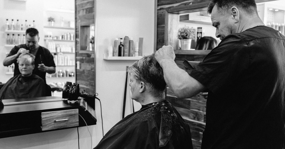 Parrucchiere taglia i capelli a una cliente seduta davanti allo specchio in un salone moderno in bianco e nero