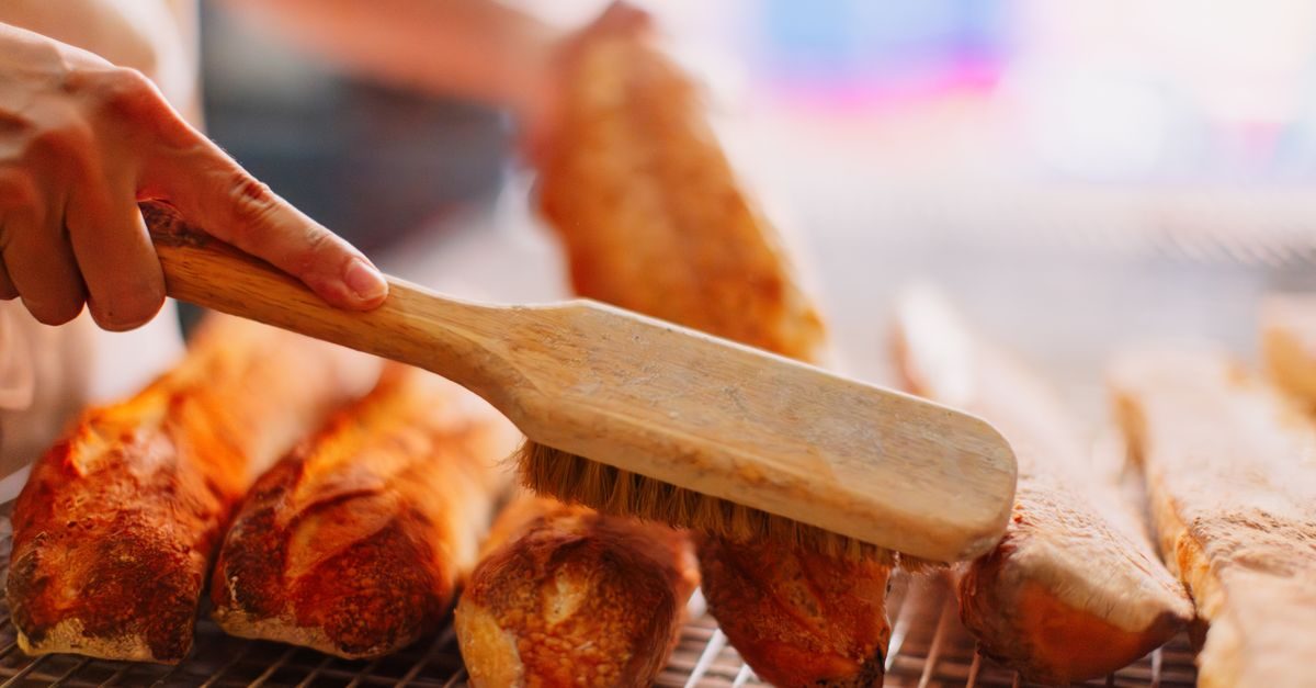 Panadero utiliza un cepillo de madera para limpiar el exceso de harina de varias barras de pan recién horneadas
