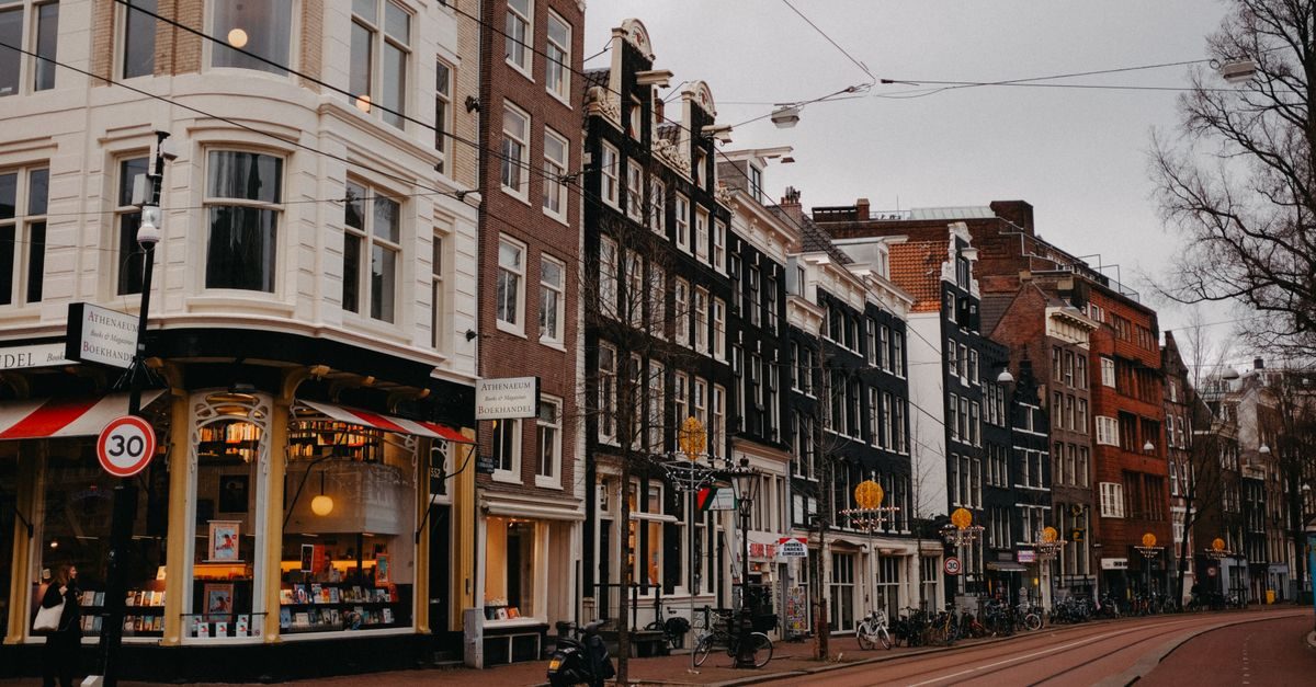 Rij van historische grachtenpanden met winkels en tramrails in een sfeervolle Amsterdamse straat op een bewolkte dag
