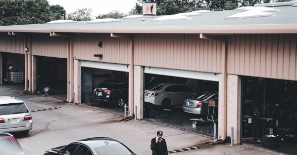 Man belt op het parkeerterrein voor een garagebedrijf met meerdere openstaande werkplaatsen waar auto's binnen staan