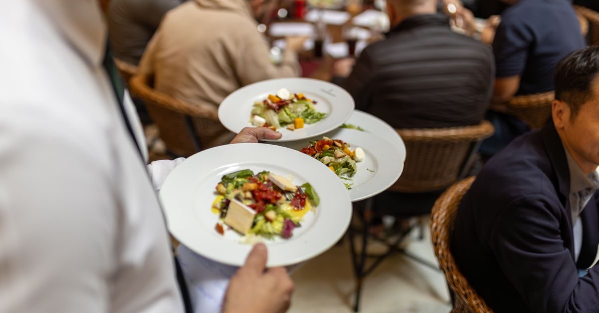 Ober serveert borden met salade aan gasten in een druk restaurant