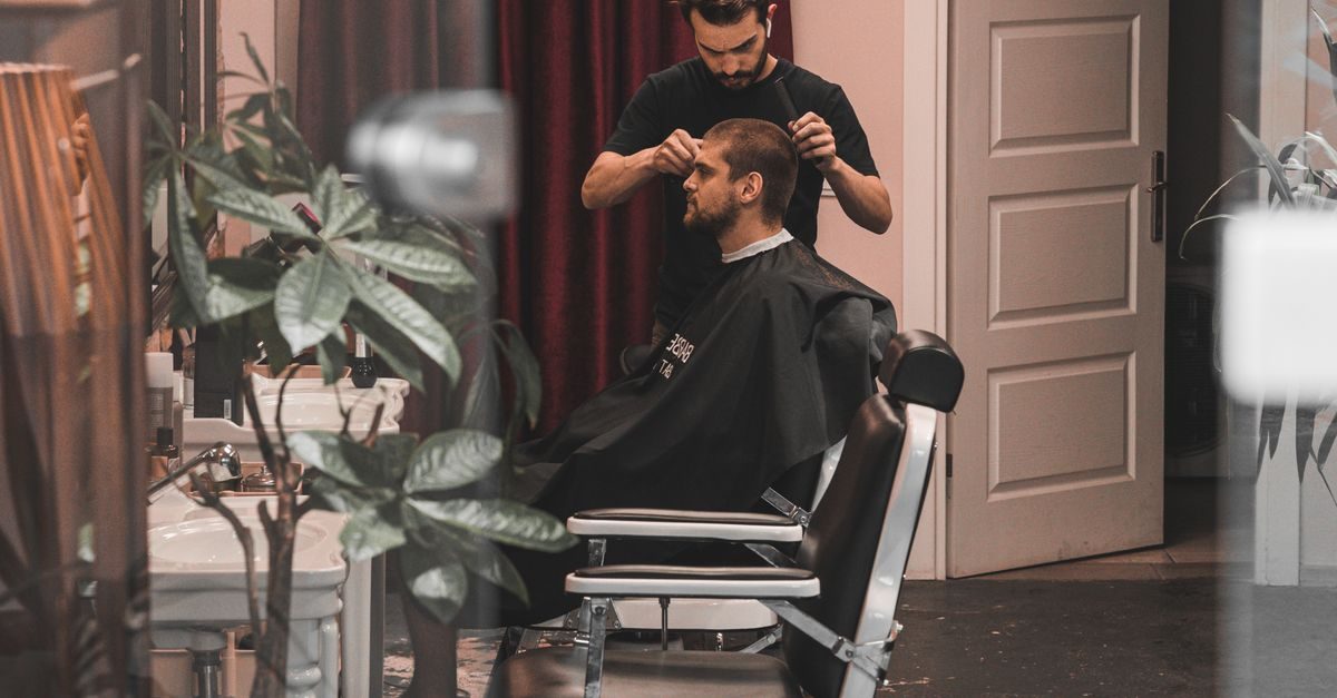 Fryzjer w czarnej koszulce strzyże brodatego klienta siedzącego w fotelu w profesjonalnym salonie fryzjerskim