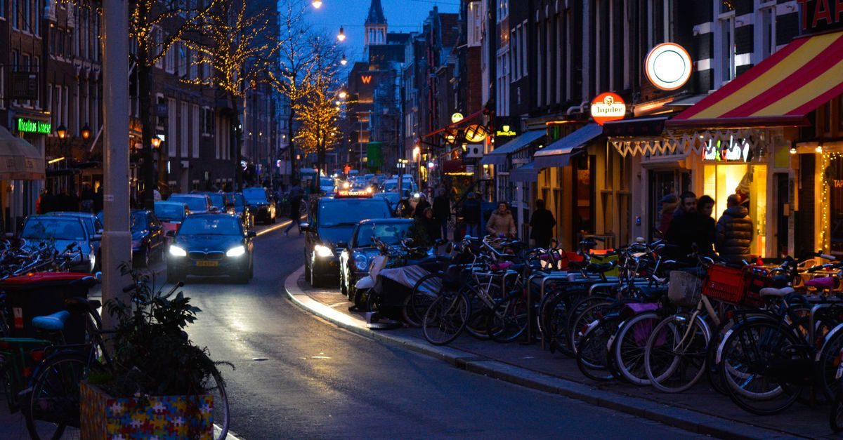 Sfeervolle avondstraat in Amsterdam met rijen geparkeerde fietsen, rijdende auto's en verlichte horecagevels