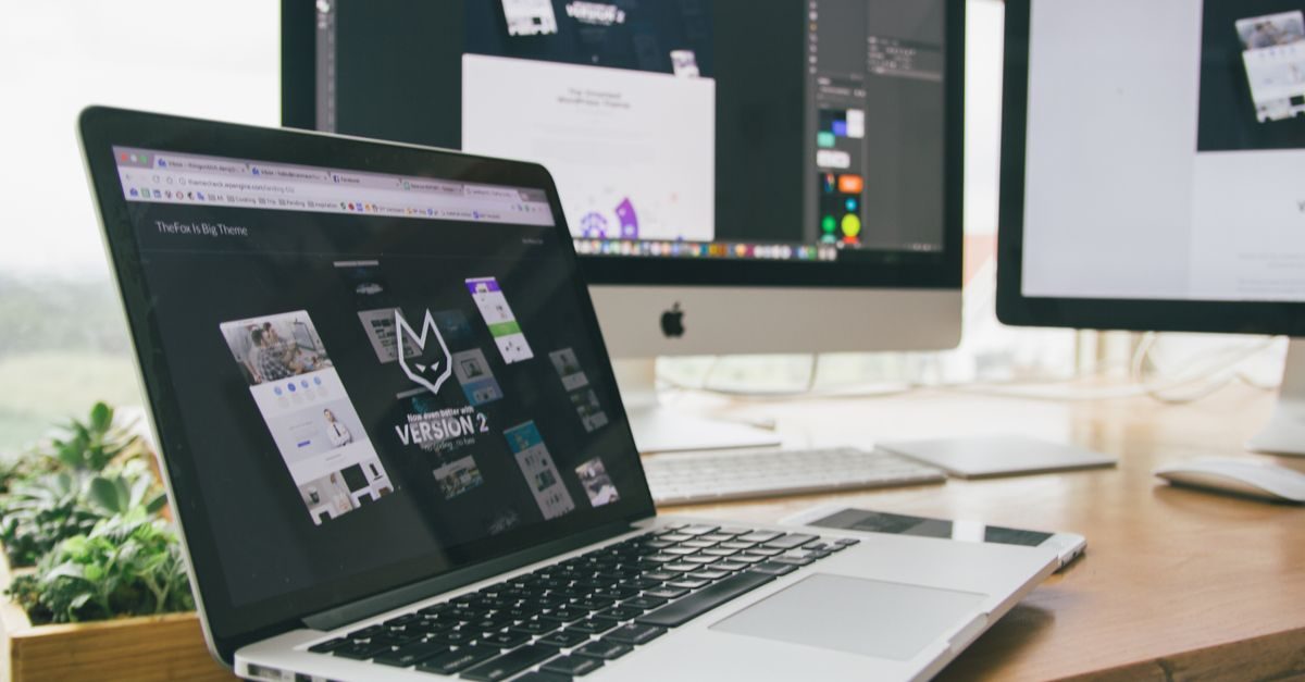 Ordinateur portable et écran de bureau affichant des interfaces web sur un bureau en bois avec une plante verte