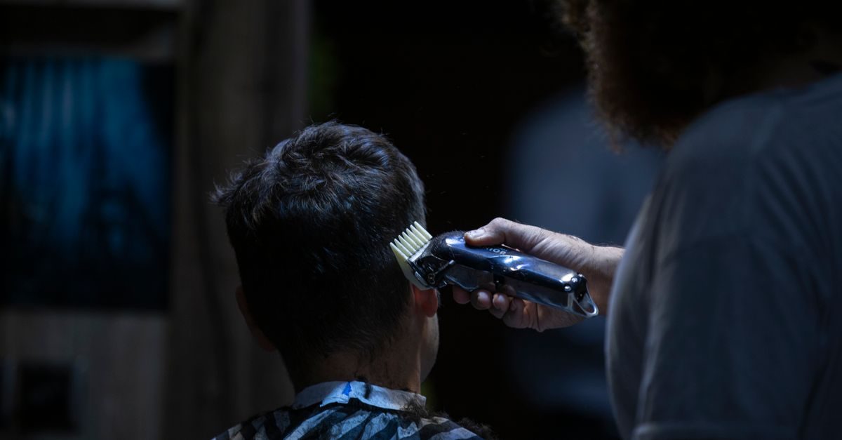 Barbero corta el cabello a un cliente con una máquina eléctrica en un ambiente de peluquería con iluminación tenue