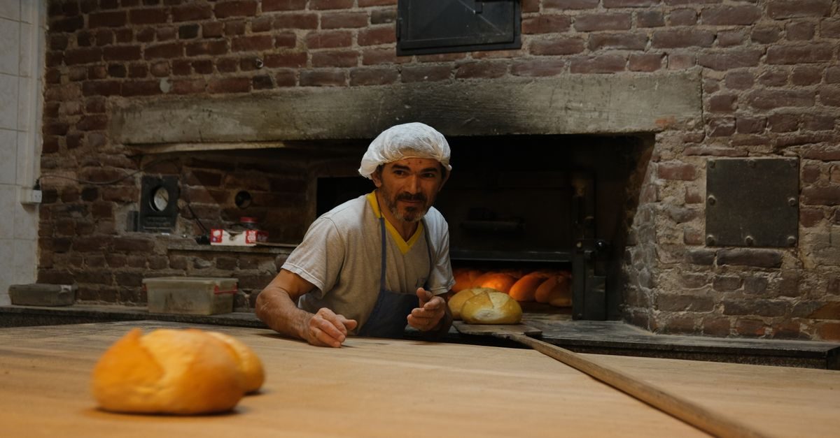 Un fornaio con cuffia e grembiule inforna il pane in un antico forno a legna in mattoni all'interno di un laboratorio