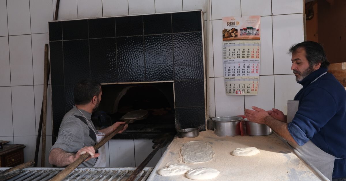 Deux boulangers travaillent dans une cuisine artisanale, l'un enfourne du pain tandis que l'autre prépare la pâte