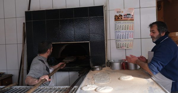 Deux boulangers travaillent dans une cuisine artisanale, l'un enfourne du pain tandis que l'autre prépare la pâte