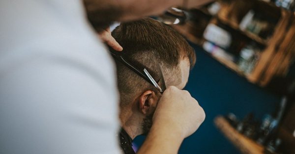 Kapper knipt met schaar en kam het haar van een man in een professionele salon