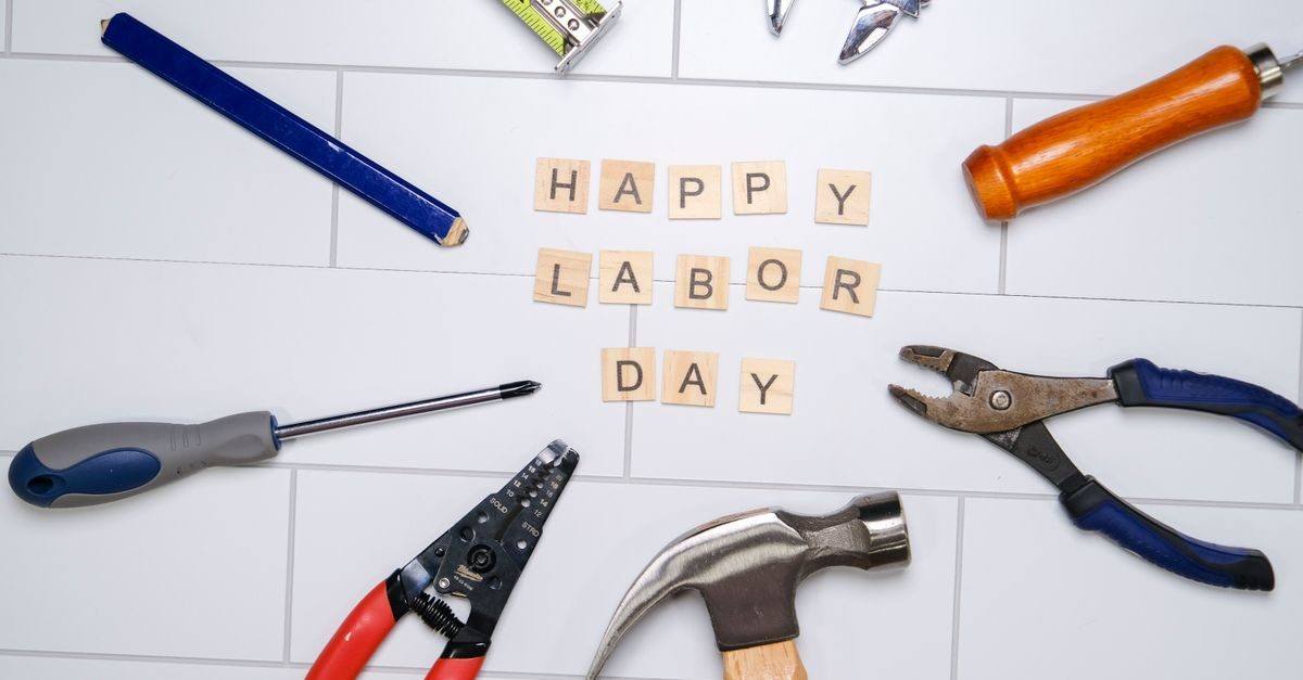 Houten letterblokjes met de tekst Happy Labor Day omringd door diverse handgereedschappen op een witte tegelvloer