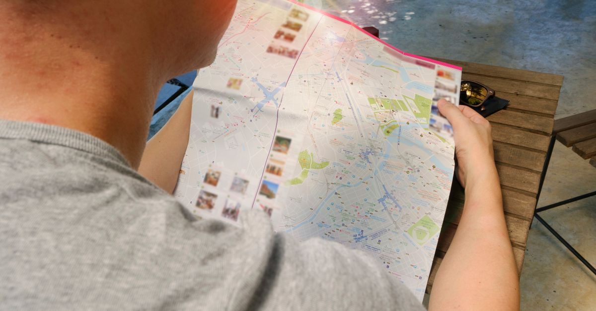 Persoon in een grijs shirt bekijkt zittend aan een houten tafel een uitgevouwen stadsplattegrond