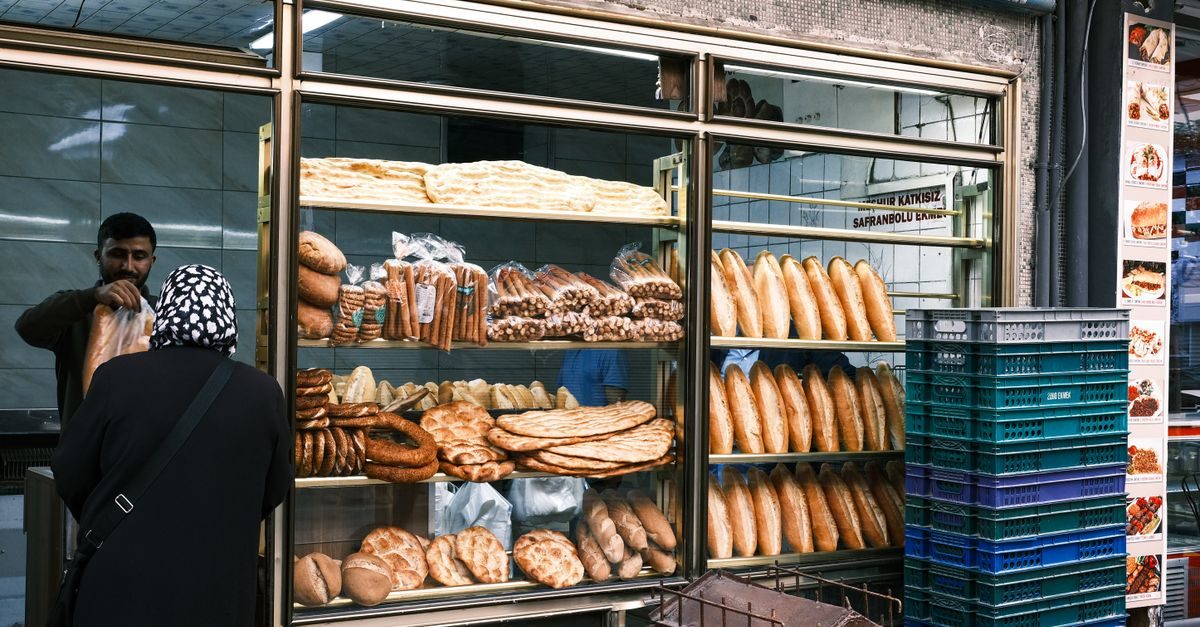 A baker serves a customer at a shop window filled with various types of fresh bread and pastries