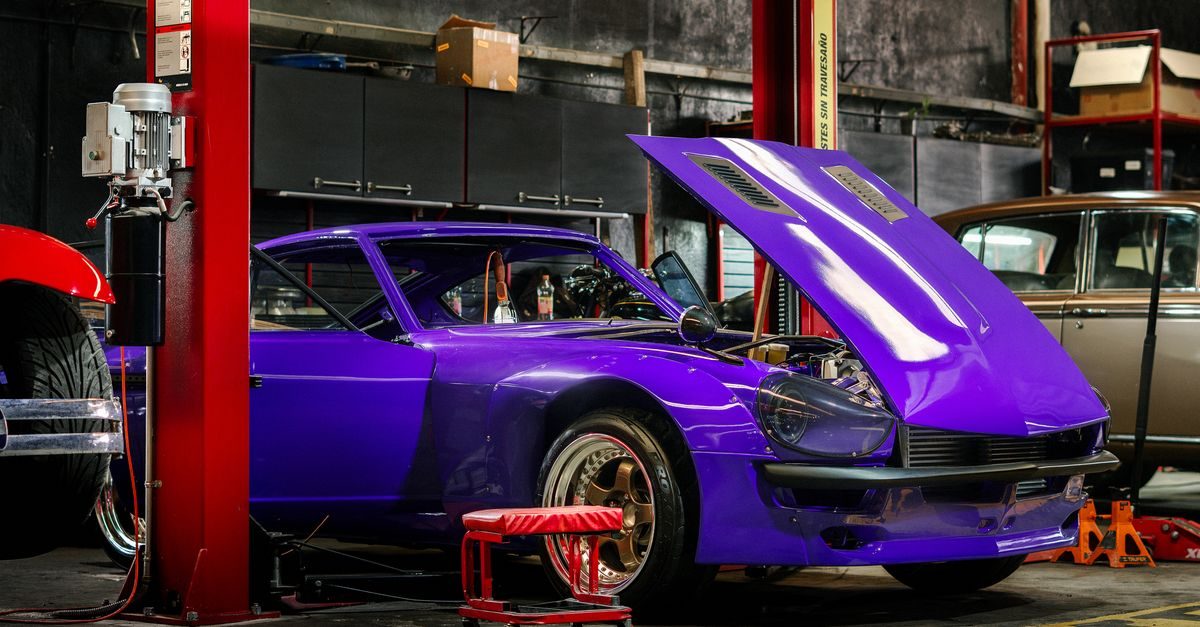 A vibrant purple sports car with its hood open sits inside a professional auto repair garage with red lift pillars