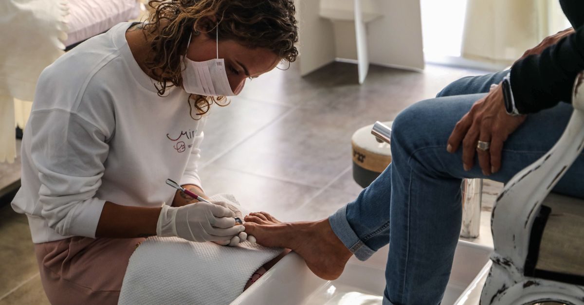 Eine Kosmetikerin mit Mundschutz und Handschuhen führt konzentriert eine professionelle Pediküre bei einer Kundin durch