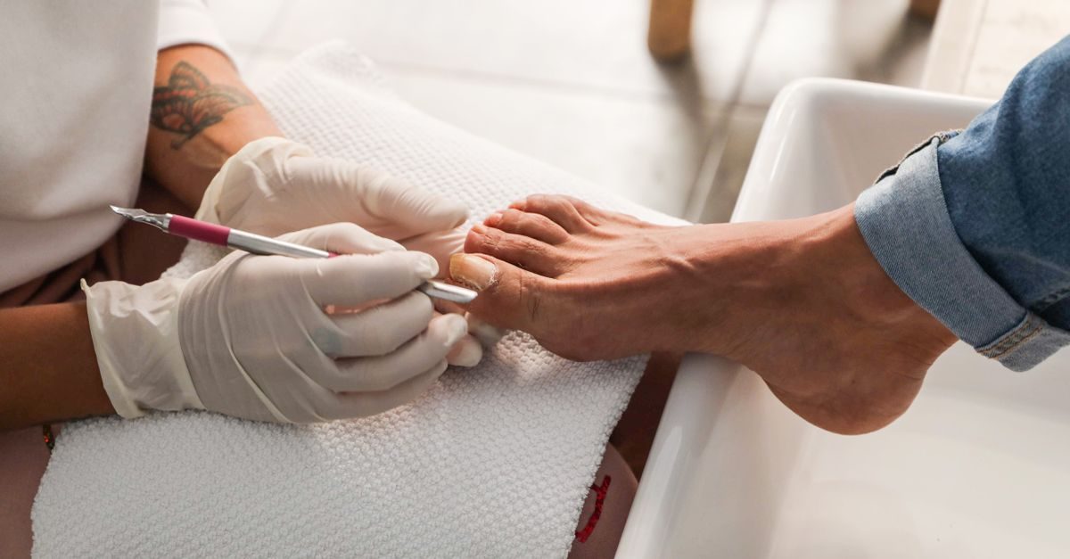 Podóloga con guantes de látex realiza una pedicura profesional a un cliente en un centro de estética especializado