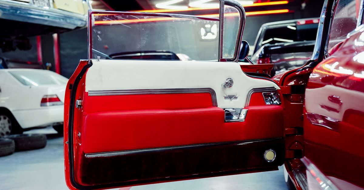 Open door of a vintage red and white car inside a brightly lit professional auto repair garage