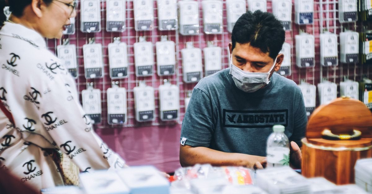 Verkoper met mondkapje helpt klant in een winkel vol verpakte producten aan de wand