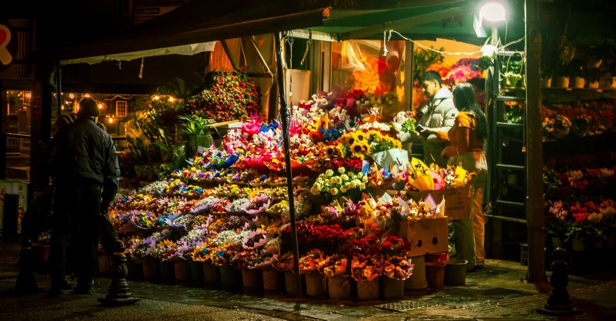 Puesto de flores nocturno con clientes y dependientes bajo una iluminación cálida en una calle urbana