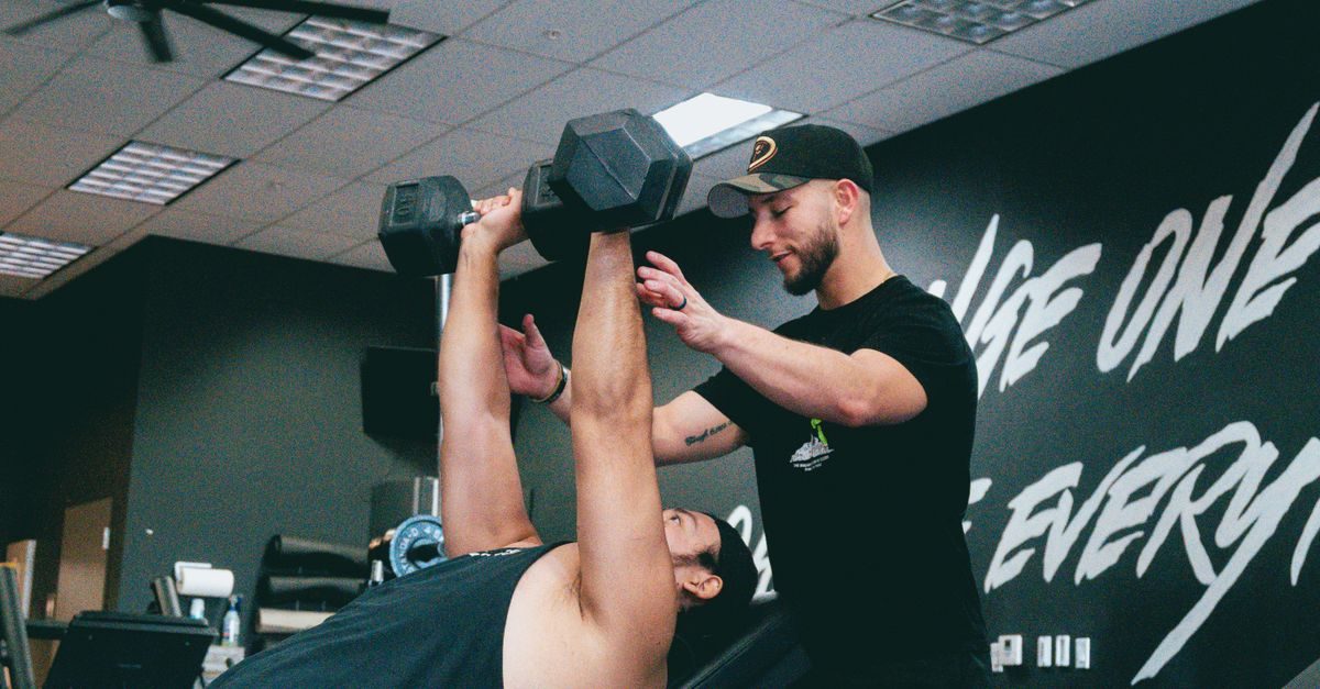 Un personal trainer segue un atleta che solleva manubri su una panca in palestra con concentrazione e impegno
