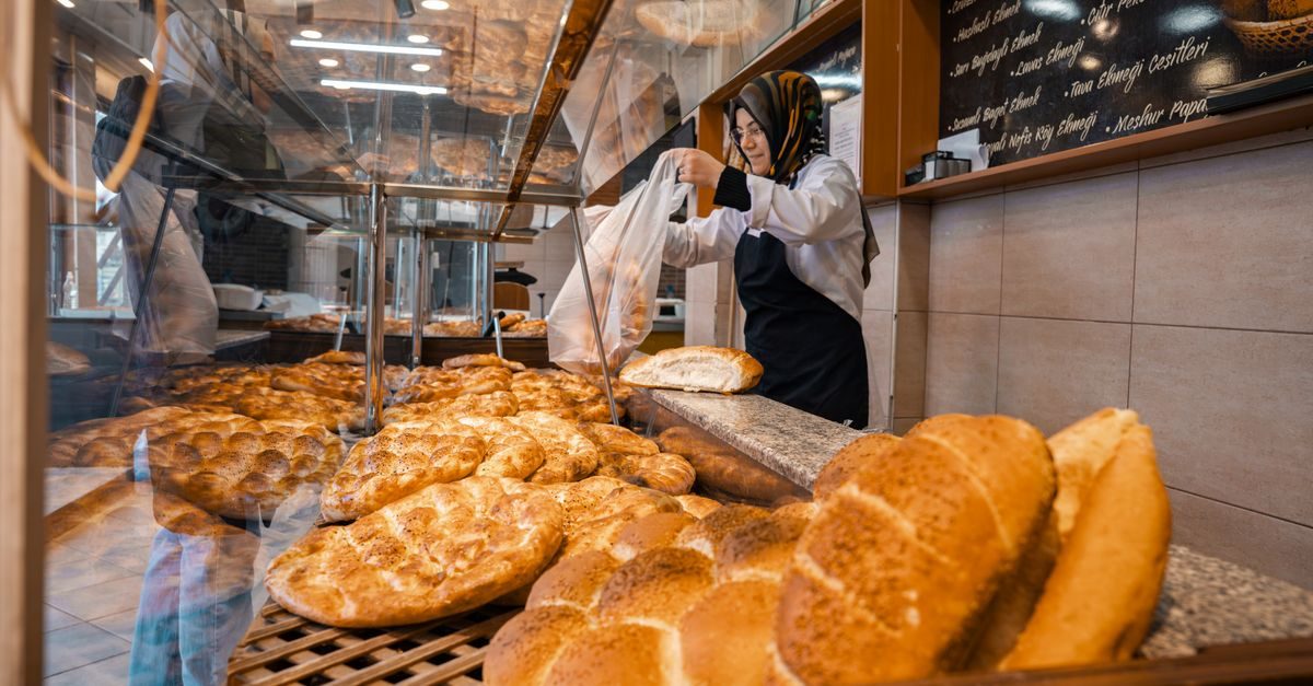 Eine Frau mit Kopftuch packt in einer Bäckerei frische Brote hinter einer Glasvitrine in eine Tüte ein