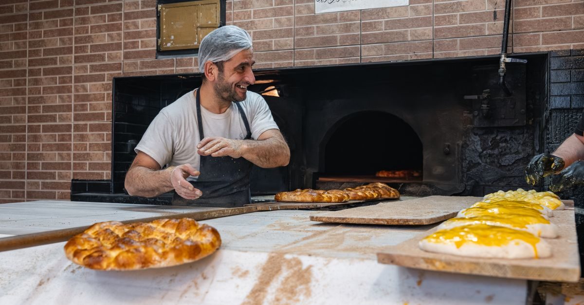 Panadero sonriente con redecilla y delantal prepara pan artesanal frente a un horno de piedra en una panadería tradicional
