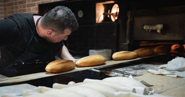 Un boulanger enfourne des pains dorés à l'aide d'une pelle en bois dans un four traditionnel sombre