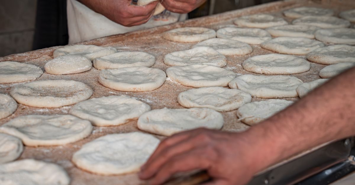 Bakker vormt met de handen deegbolletjes op een met bloem bestoven werkblad in een bakkerij