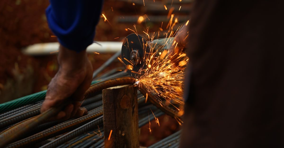 Un trabajador corta varillas de metal con una amoladora, generando chispas brillantes en una obra de construcción
