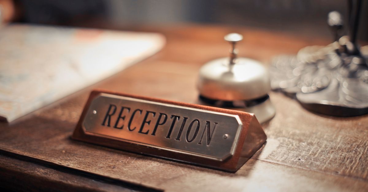 Metalen receptiebordje met een hotelbel op een houten balie in een sfeervolle hotelomgeving