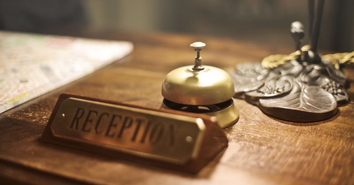 Mosiężny dzwonek hotelowy i tabliczka z napisem Reception na drewnianym blacie lady recepcyjnej w ciepłym oświetleniu