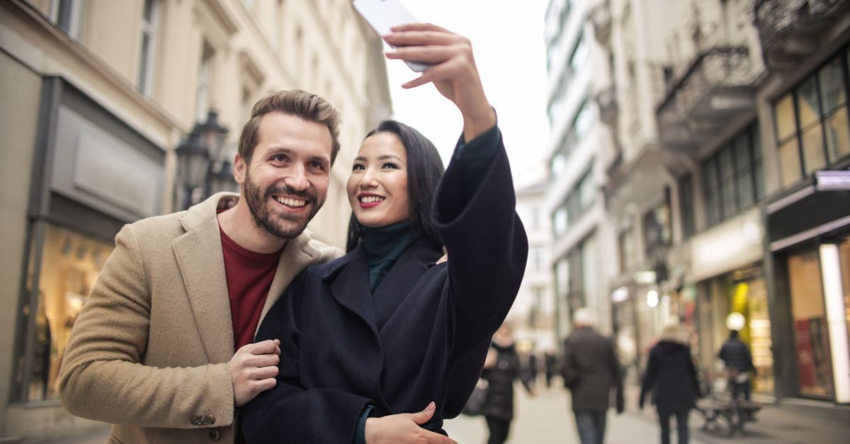 Uśmiechnięta para robi sobie selfie telefonem na tle miejskiej ulicy z witrynami sklepowymi